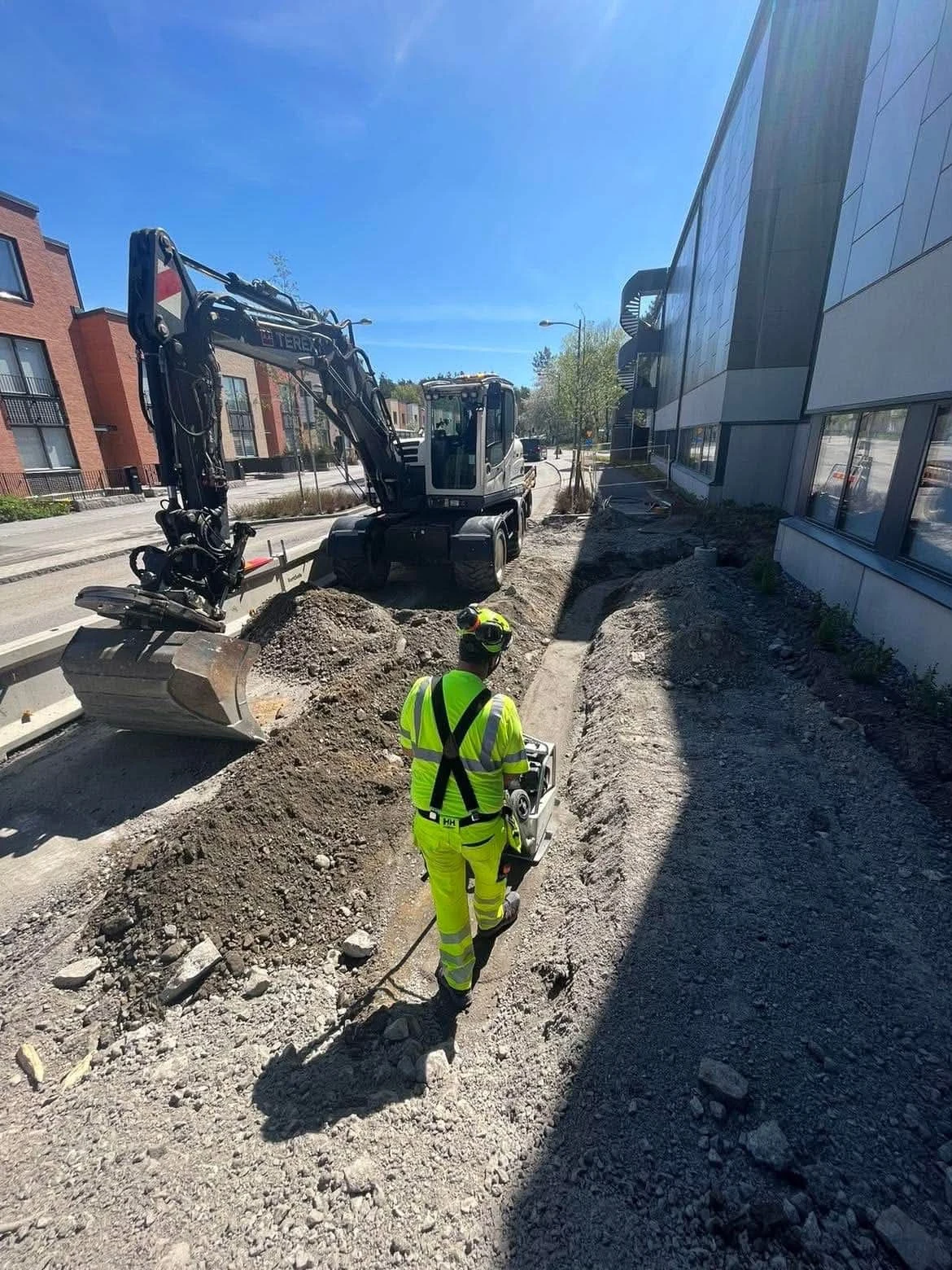 Grävmaskin arbetar i en avgränsad schakt i stadsmiljö
